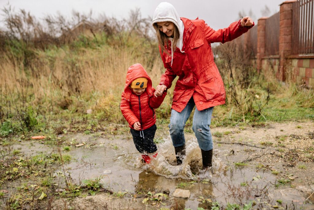 A cheerful mother and child splash in a puddle on a rainy day, both wearing red jackets.